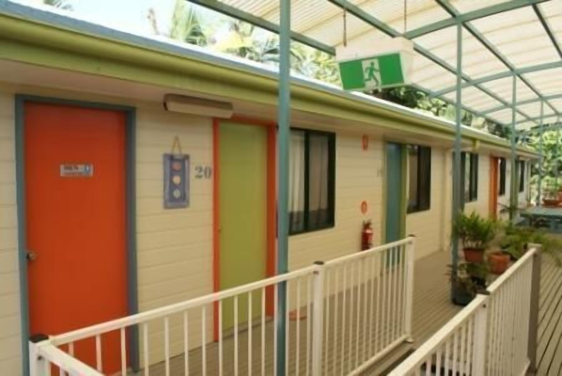 A row of motel rooms with numbered doors, a balcony with railings, and a green emergency exit sign.
