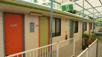 Fileira de quartos de motel com portas numeradas, uma varanda com grades e um sinal de saída de emergência verde.