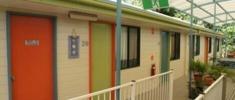 A row of motel rooms with numbered doors, a balcony with railings, and a green emergency exit sign.