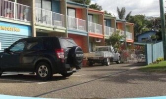 Una hilera de edificios coloridos con balcones, un SUV negro estacionado al frente y un camión detrás.