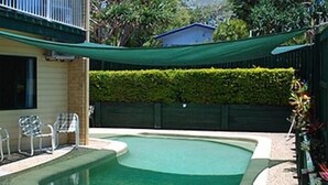 A swimming pool with a curved edge, surrounded by a pebble border. There are two lounge chairs and a small table near the pool.