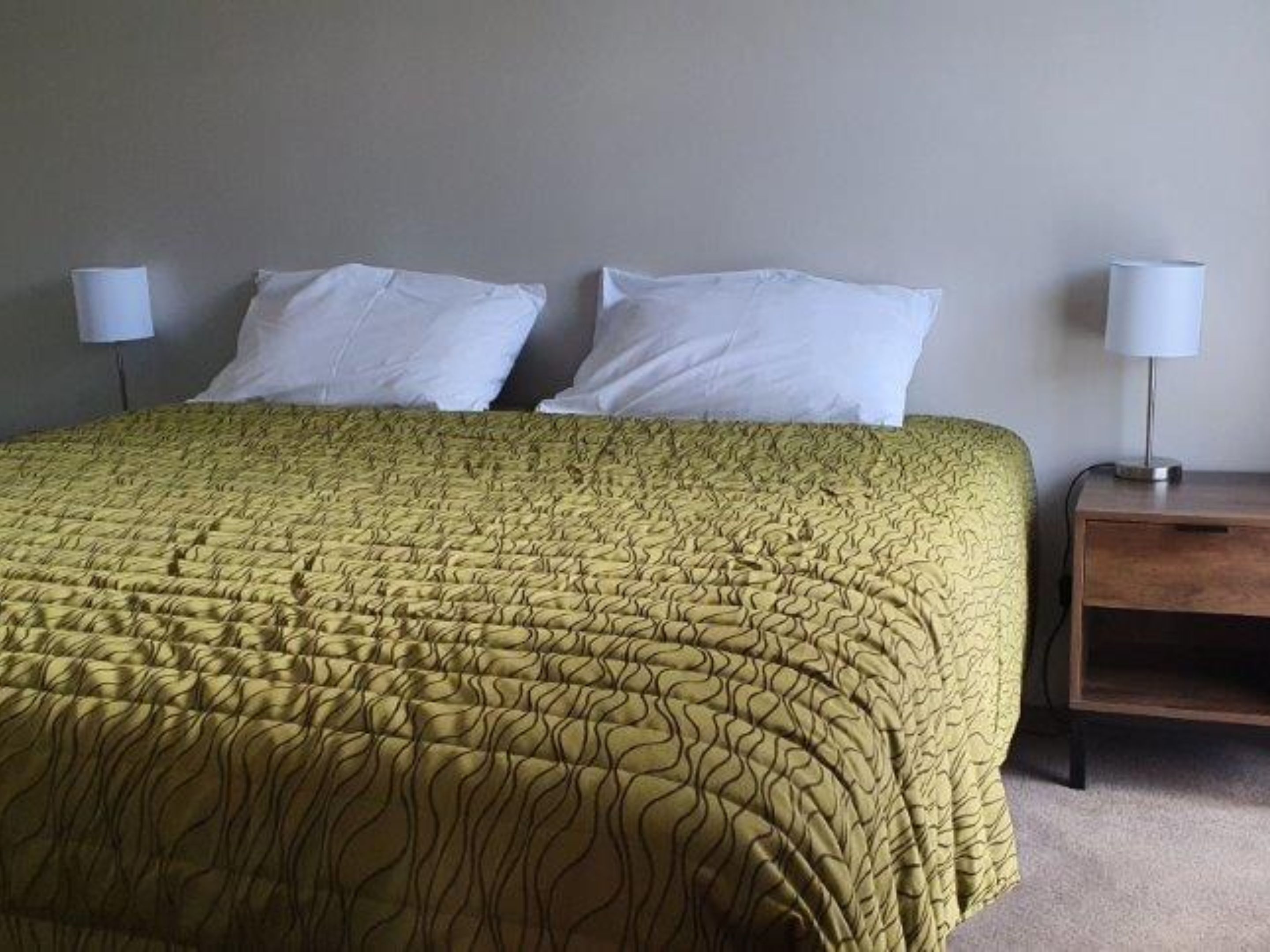 A bed with a patterned bedspread, two white pillows, and a nightstand with a lamp.