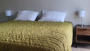 Una cama con una colcha estampada, dos almohadas blancas y una mesita de noche con una lámpara.