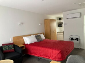 A hotel room with a bed, a desk, a chair, a wardrobe, a microwave, and an air conditioning unit. - Ashburton's Regency Motel (Ashburton)