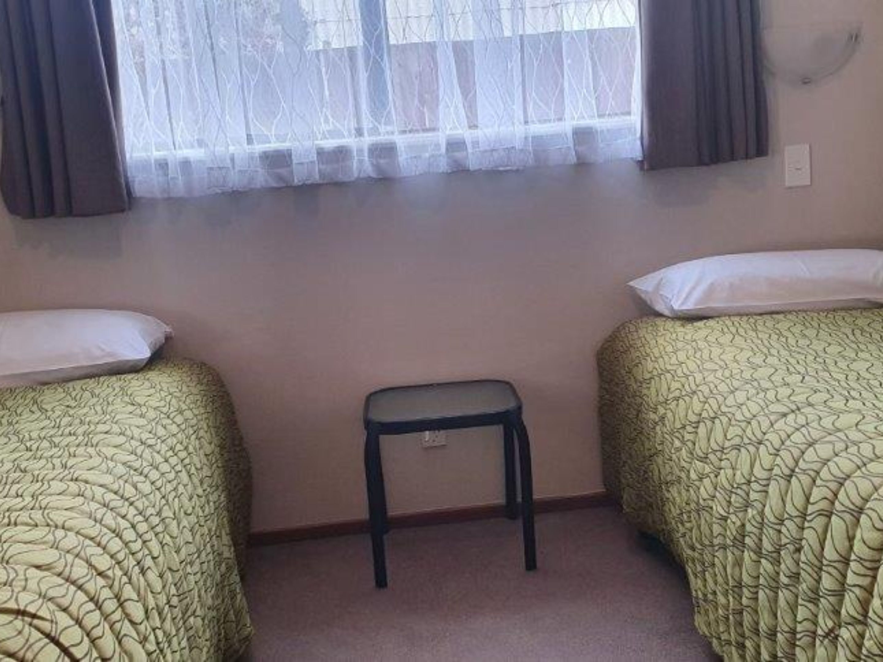 Una habitación con dos camas, una mesita y un ventanal con cortinas.