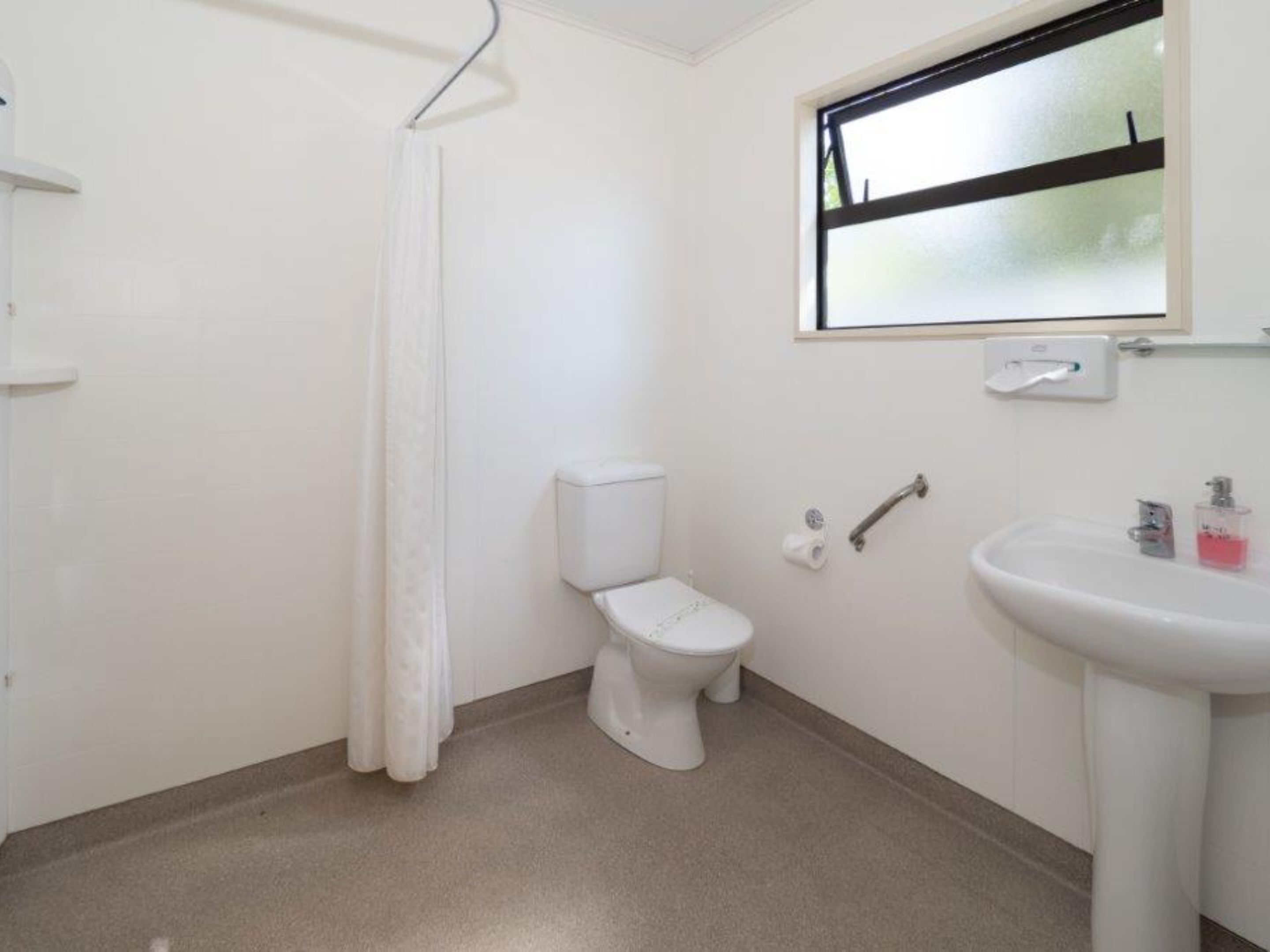 Un baño pequeño y limpio, con inodoro, lavamanos y cortina de ducha.