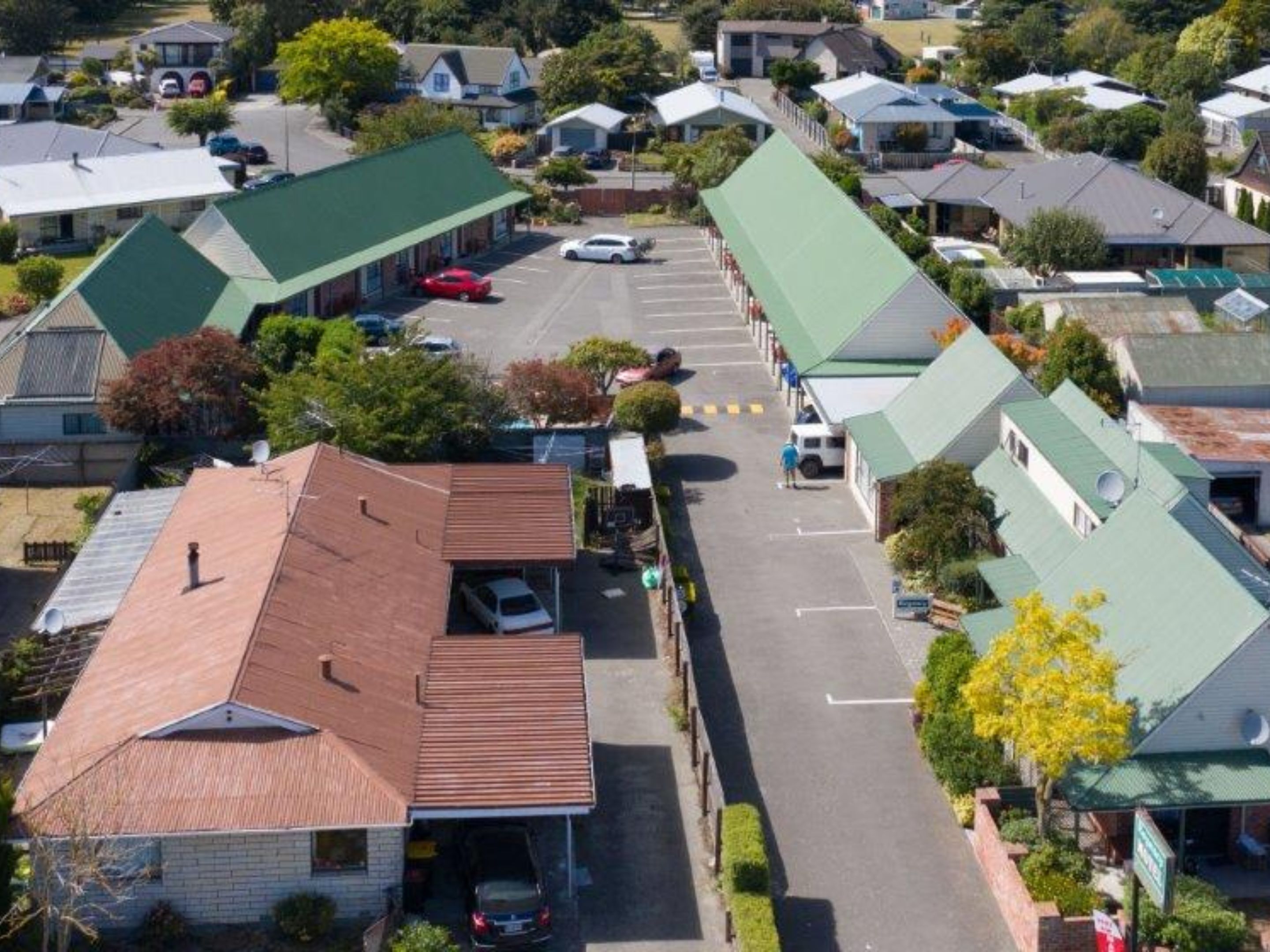 A residential street with houses, a parking lot, and a small commercial building with a green roof.