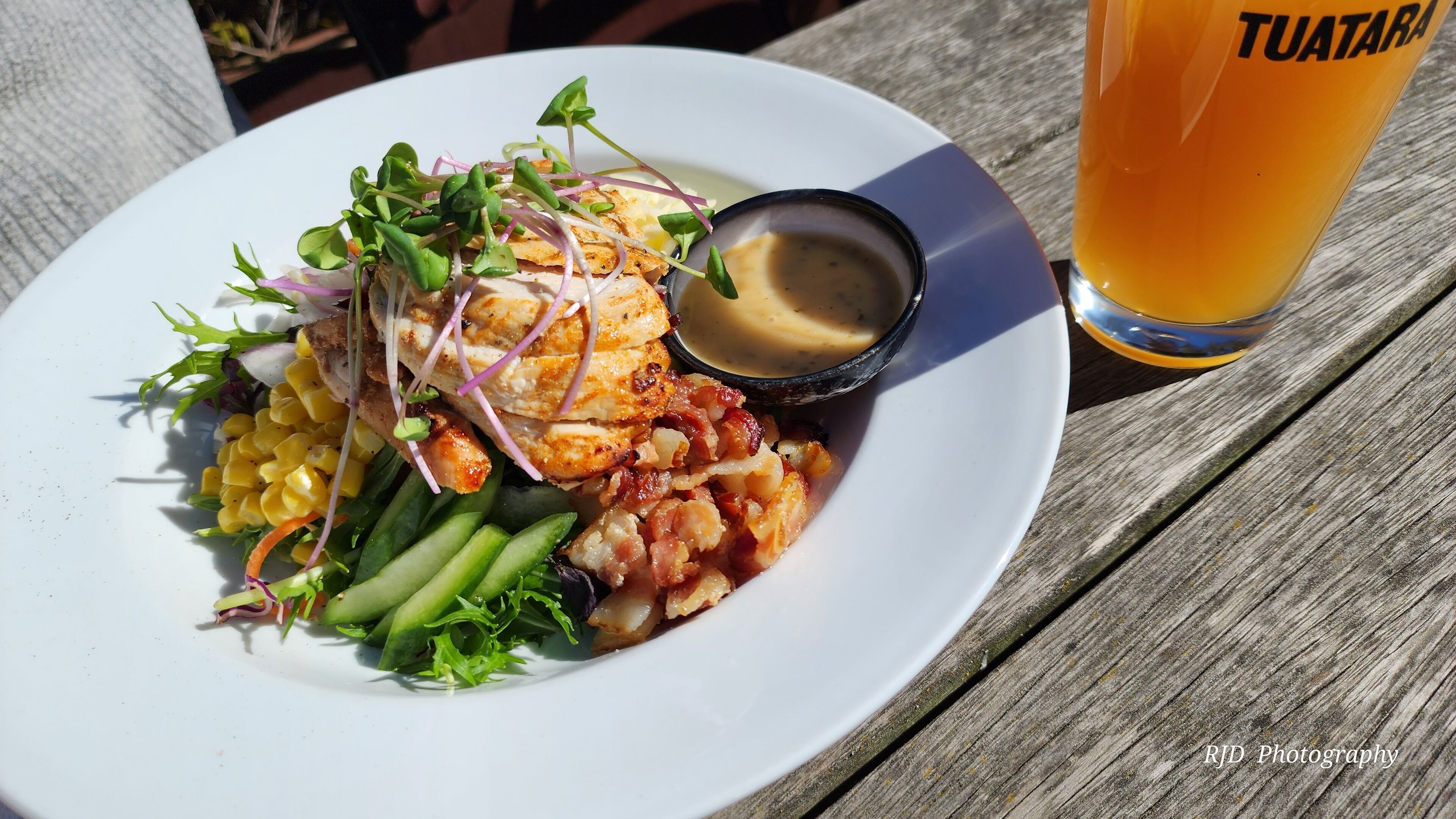 A plate of food with a side of sauce and a glass of beer on a wooden table.
