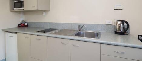 A compact kitchen with a sink, kettle, and microwave.