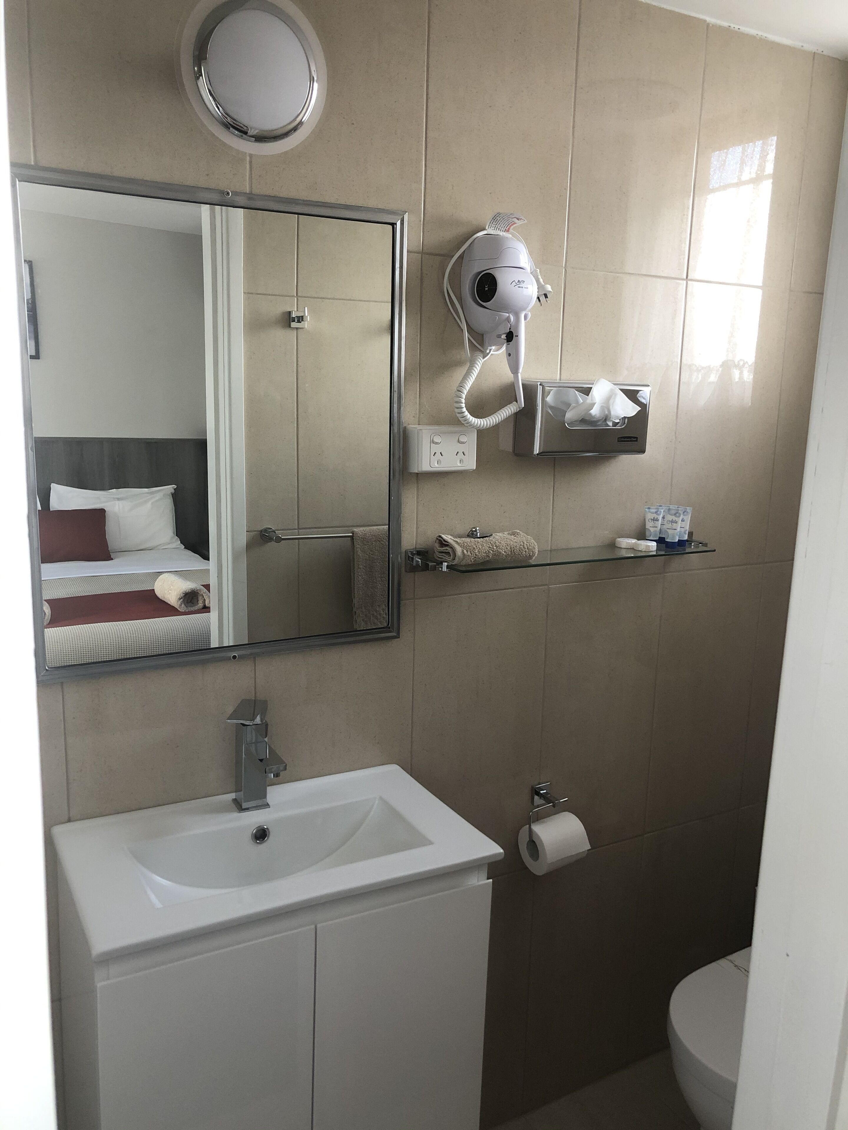 A bathroom with a sink, mirror, hairdryer, towel rack, and toilet.