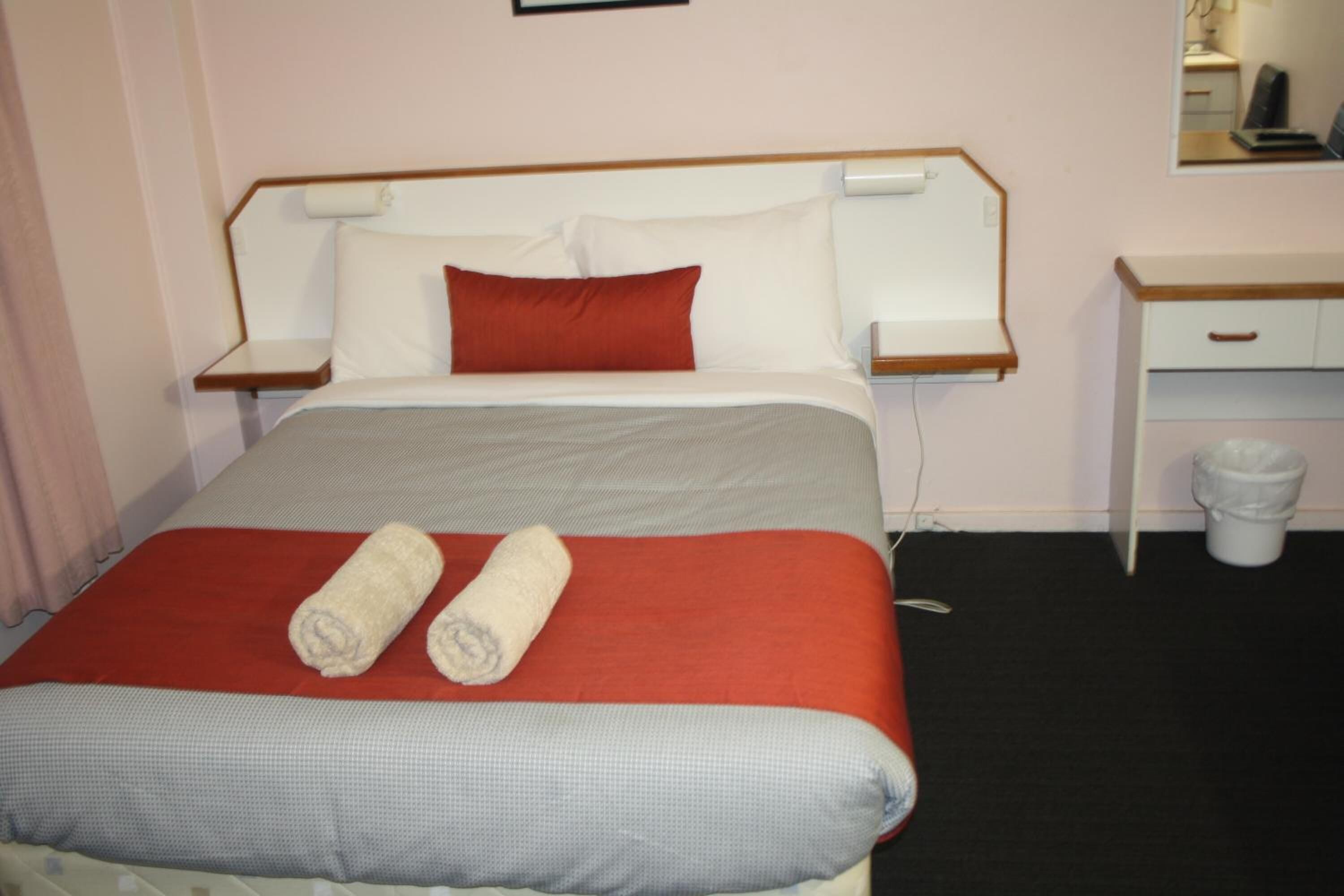 Una habitación de hotel con cama, mesita de noche, escritorio y un cesto de basura.