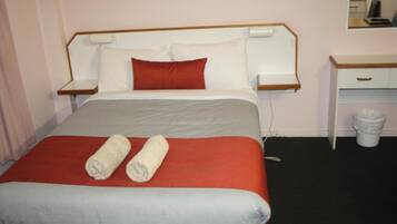Una habitación de hotel con cama, mesita de noche, escritorio y un cesto de basura.
