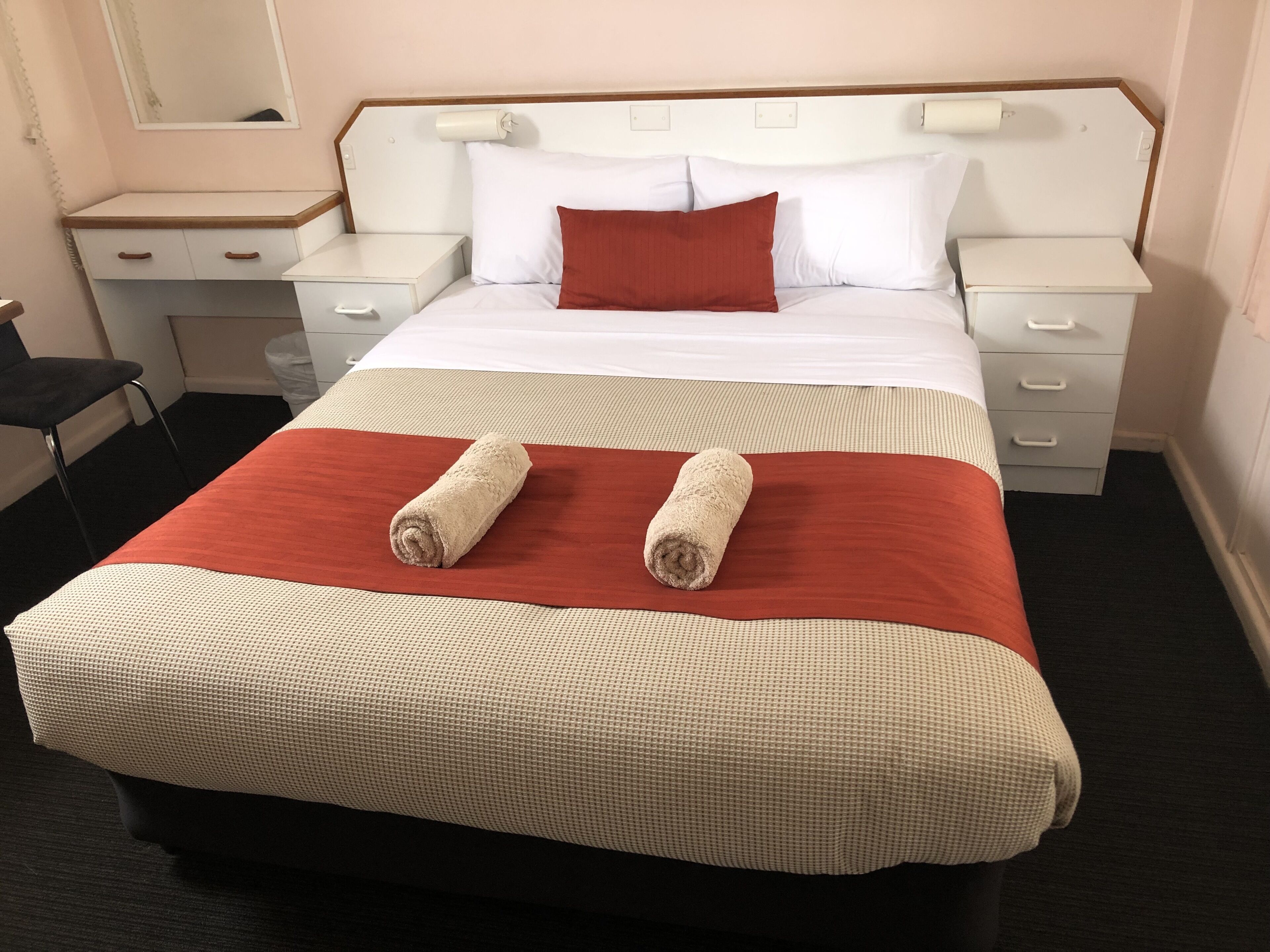 A hotel room with a neatly made bed, two bedside tables, a chair, and a mirror on the wall.