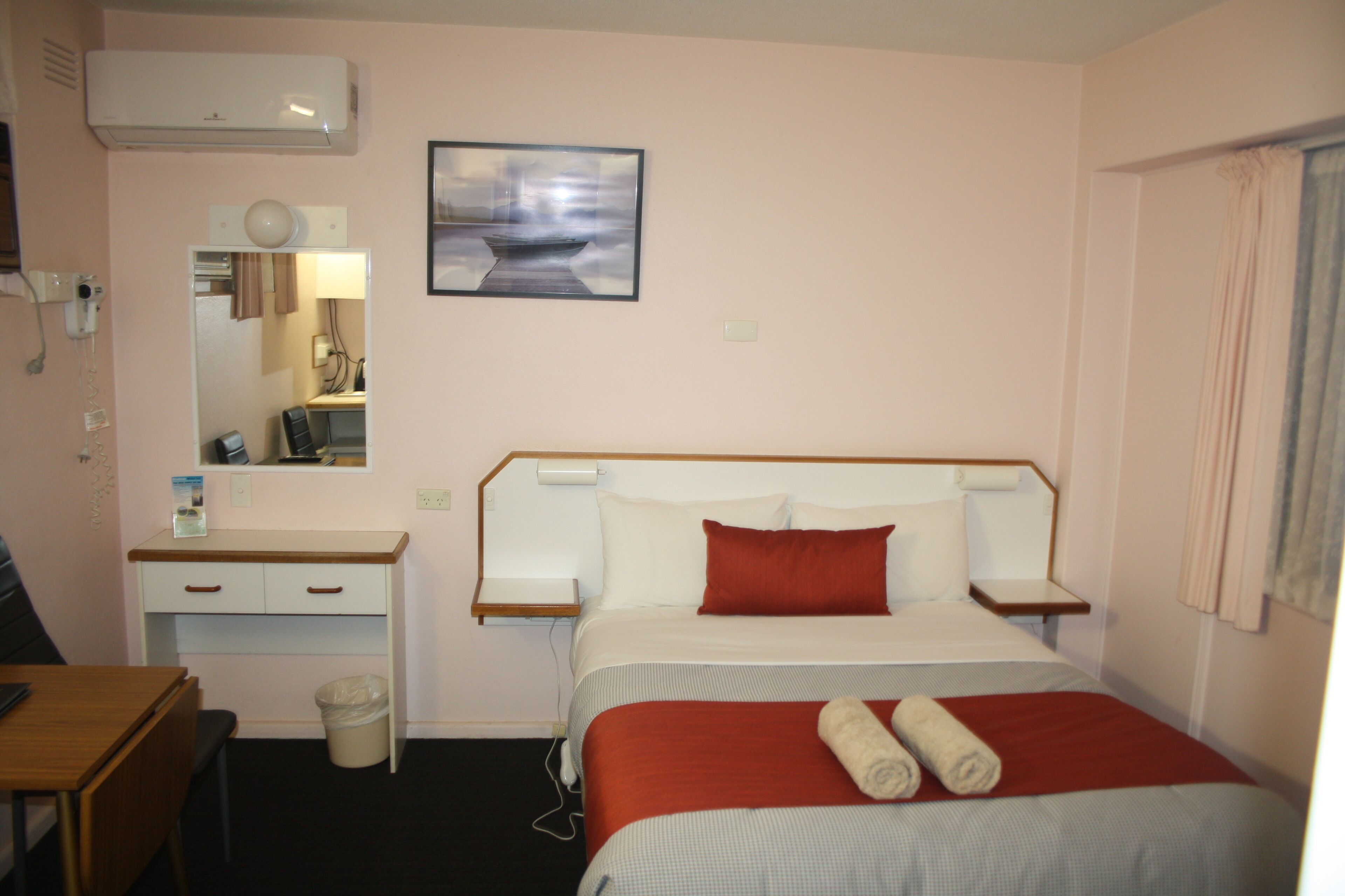 Une chambre d ’hôtel équipée d’un lit, d’un bureau, d’une chaise, d’une poubelle et d’un climatiseur fixé au mur.