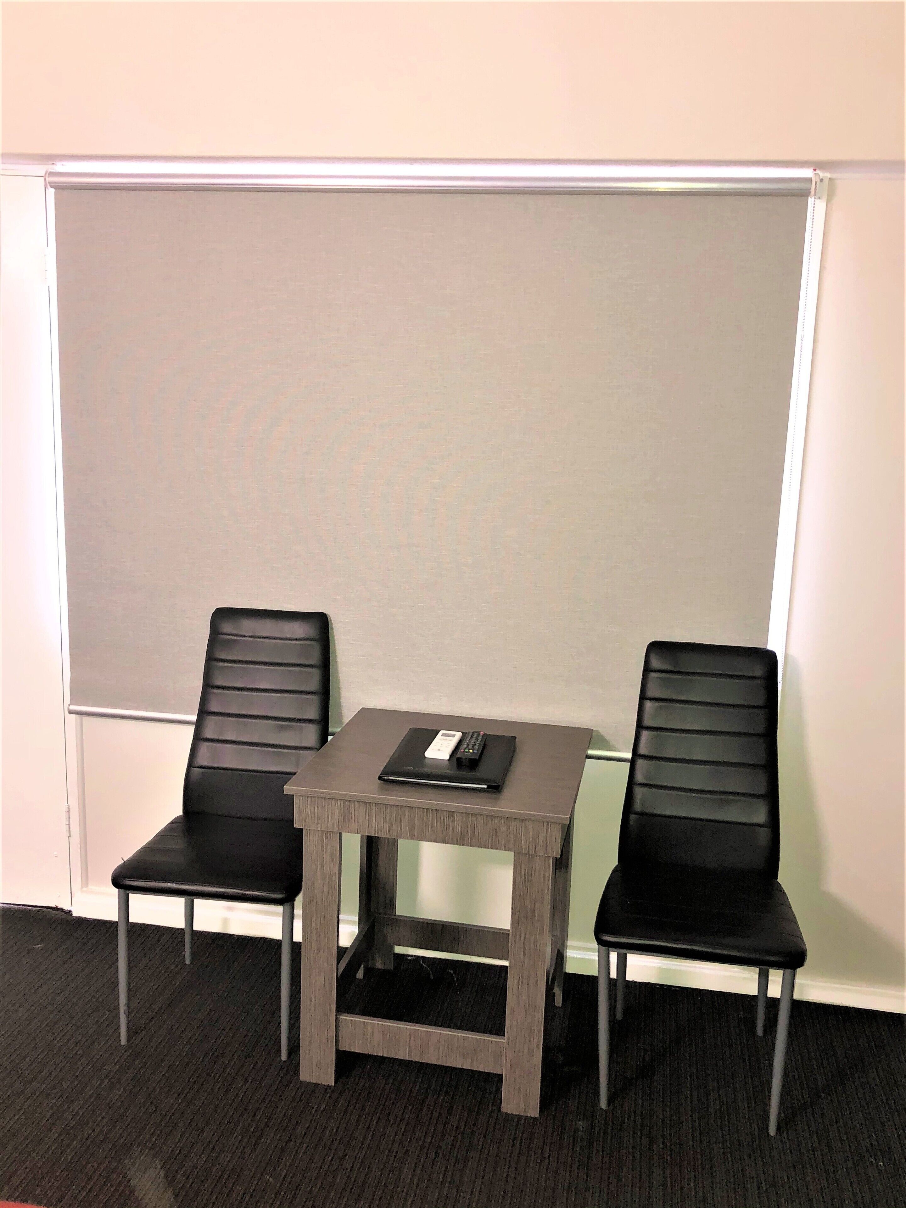 Ein Zimmer mit einem kleinen Tisch, zwei Stühlen, einer Whiteboard und einem Teppichboden.