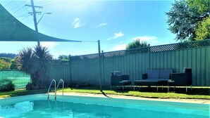 A rectangular swimming pool with a ladder, surrounded by a wooden fence, and a patio area with outdoor furniture. - Bradman Motor Inn (Cootamundra)