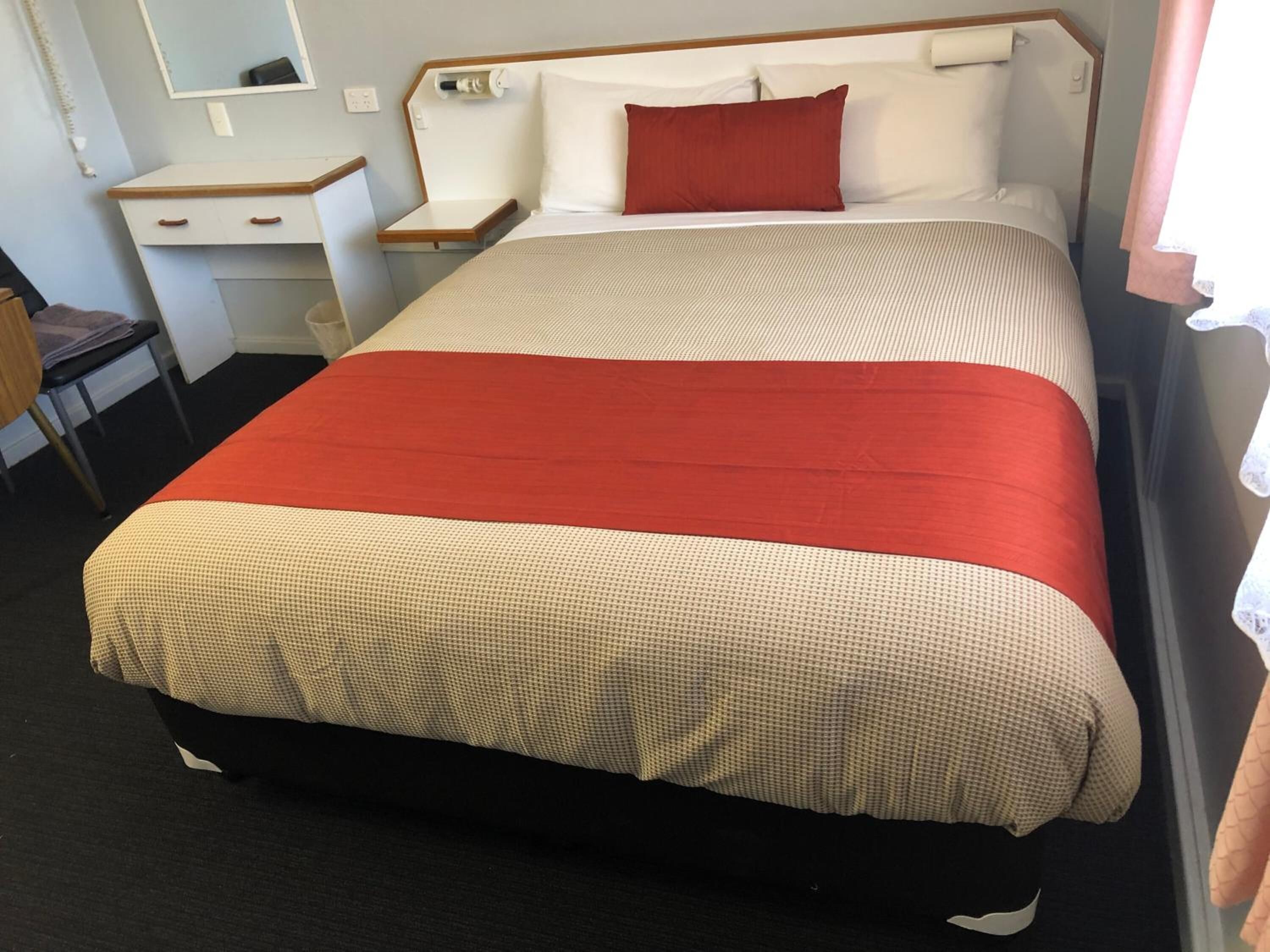 A hotel room with a bed, a bedside table, a chair, and a mirror.