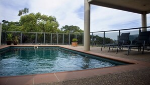 Una piscina con vistas a árboles y una zona cubierta con sillas.