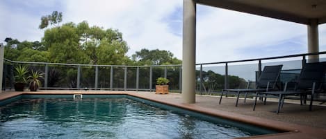 A swimming pool with a view of trees and a covered area with chairs.