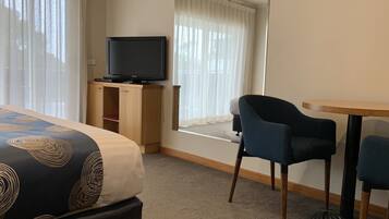 A hotel room with a bed, a television on a wooden cabinet, a window with curtains, and a small table with two chairs.