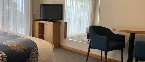 A hotel room with a bed, a television on a wooden cabinet, a window with curtains, and a small table with two chairs.