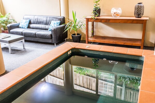 Una sala de estar con un sofá de cuero gris, una mesita de centro pequeña, una mesita auxiliar de madera con objetos decorativos y una piscina interior pequeña.