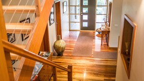 Una escalera de madera que conduce a una habitación con un ventanal grande, un tapete y un jarrón en el suelo.