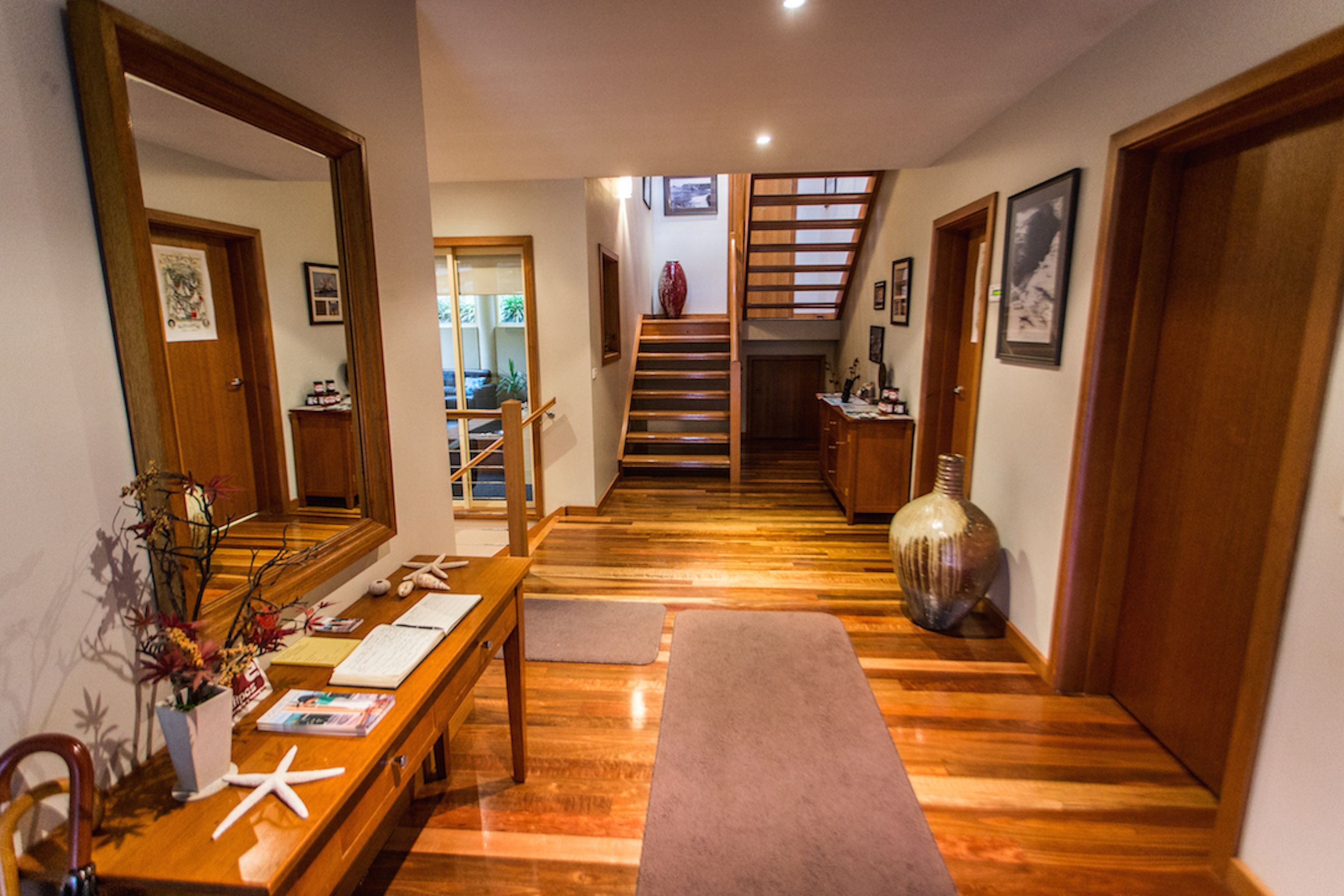 Un pasillo con un banco de madera, un espejo grande, un florero y una escalera que lleva a otra habitación.