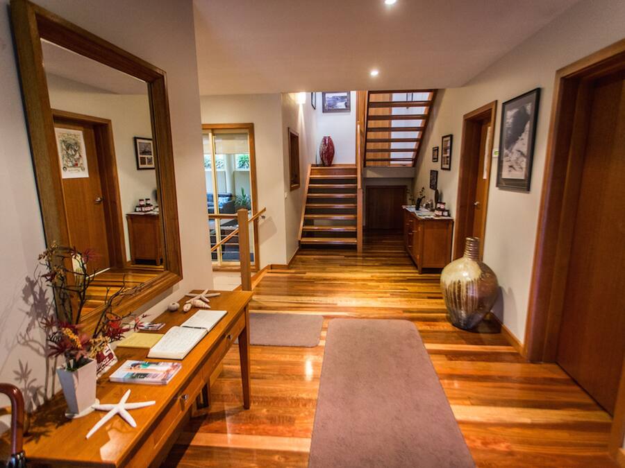 Un pasillo con un banco de madera, un espejo grande, un florero y una escalera que lleva a otra habitación.