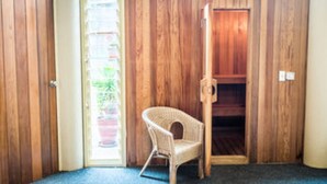 Una habitación con paredes de paneles de madera, una silla de mimbre y una puerta que da a un espacio exterior.