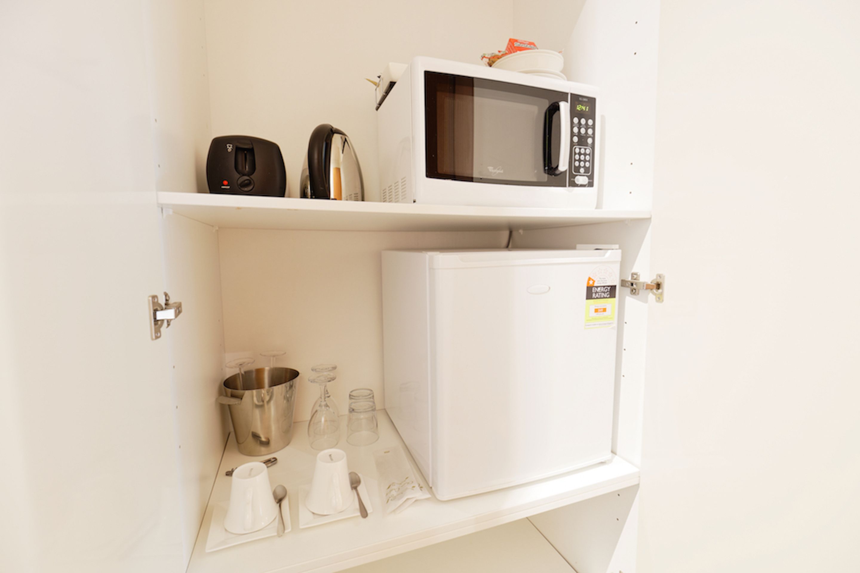 Een kitchenette met een magnetron, een minibar en een plank met een waterkoker en een koffiezetapparaat.