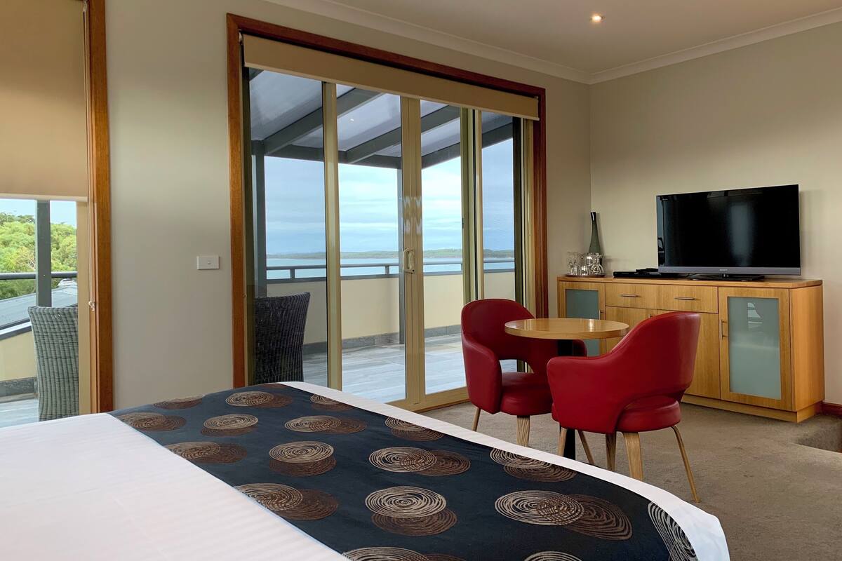 Ein Hotelzimmer mit Bett, Fernseher, Esstisch mit Stühlen und einem Balkon mit Blick.
