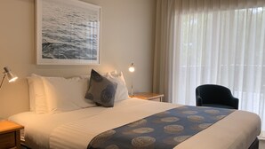 Una cama bien hecha con una colcha estampada, un almohadón con un diseño circular, una lámpara de noche y un cuadro en la pared.