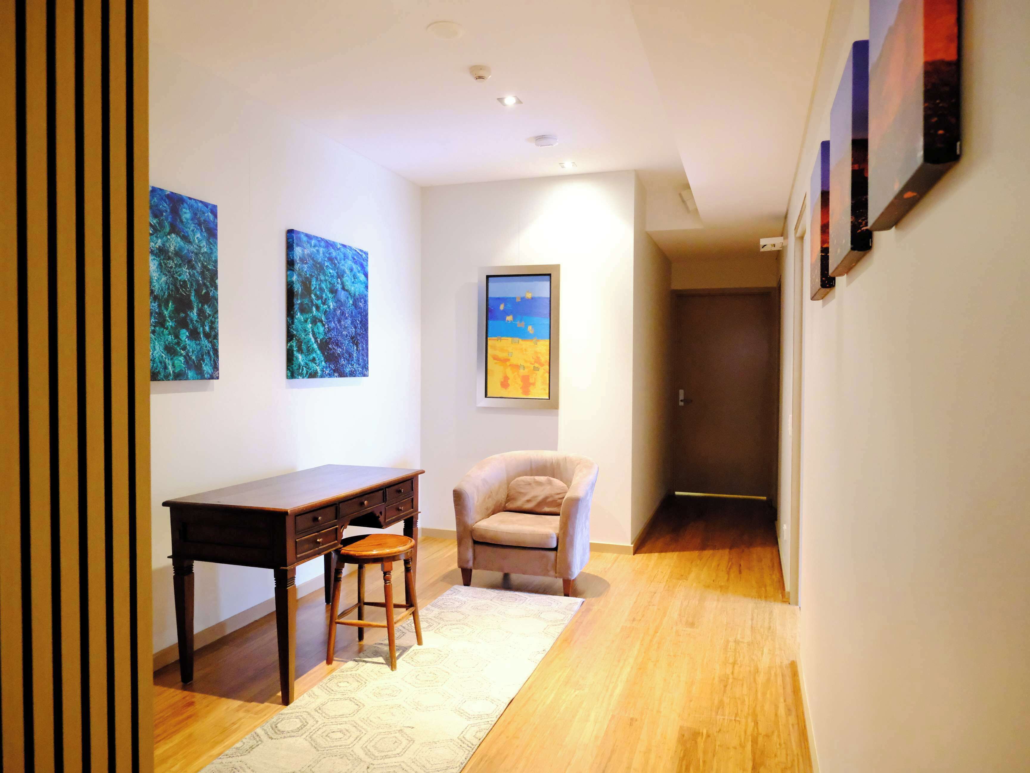 A hallway with a wooden desk, two stools, and three paintings on the walls.