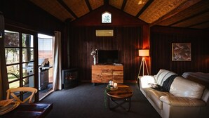 Un interior de cabaña acogedor, con chimenea, paredes de madera, televisor y sofá.