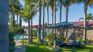 A backyard with a covered patio, a pool, and a fenced area. - Sandbar Motel (Lakes Entrance)