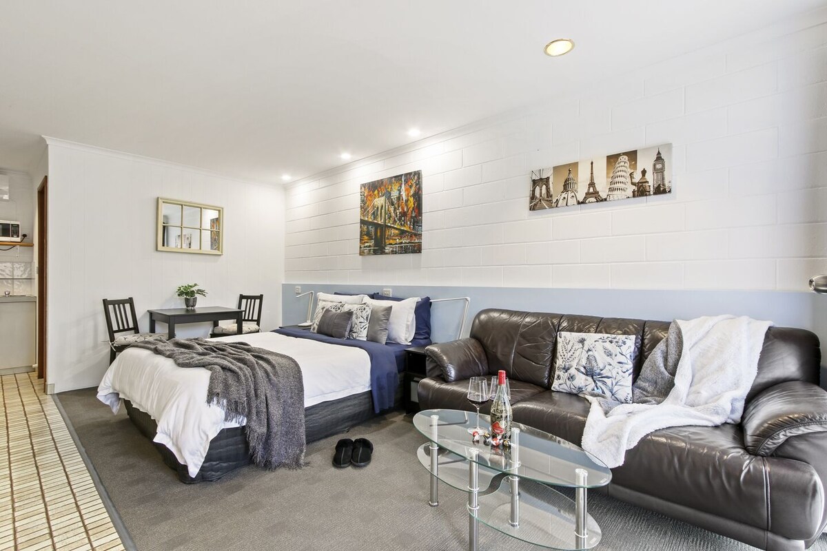 A modern bedroom with a bed, a leather sofa, a glass coffee table, and a dining area with a table and chairs.