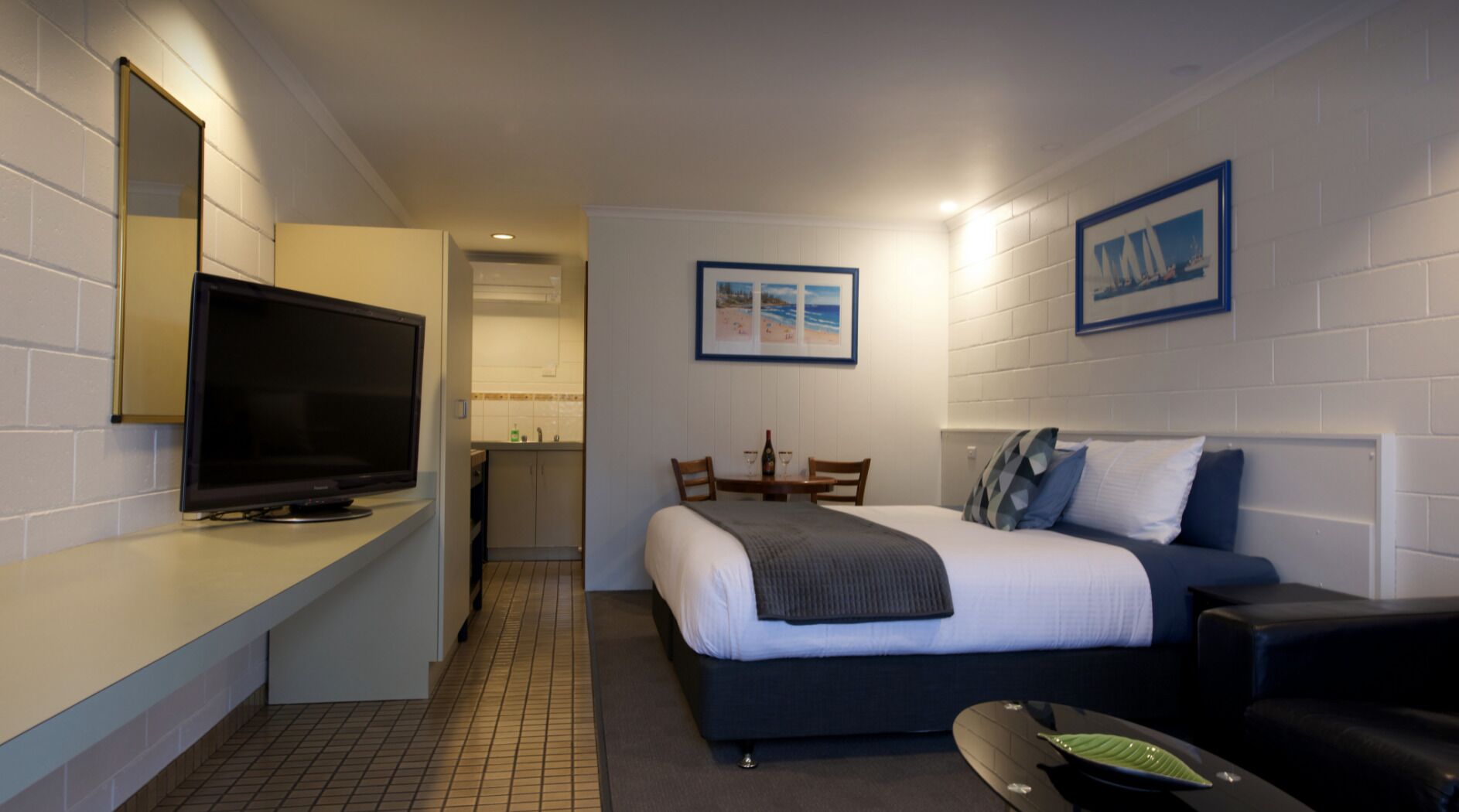 Una habitación de hotel compacta con cama, televisor, kitchenette pequeña y comedor.