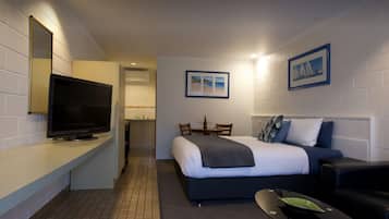 Una habitación de hotel compacta con cama, televisor, kitchenette pequeña y comedor.