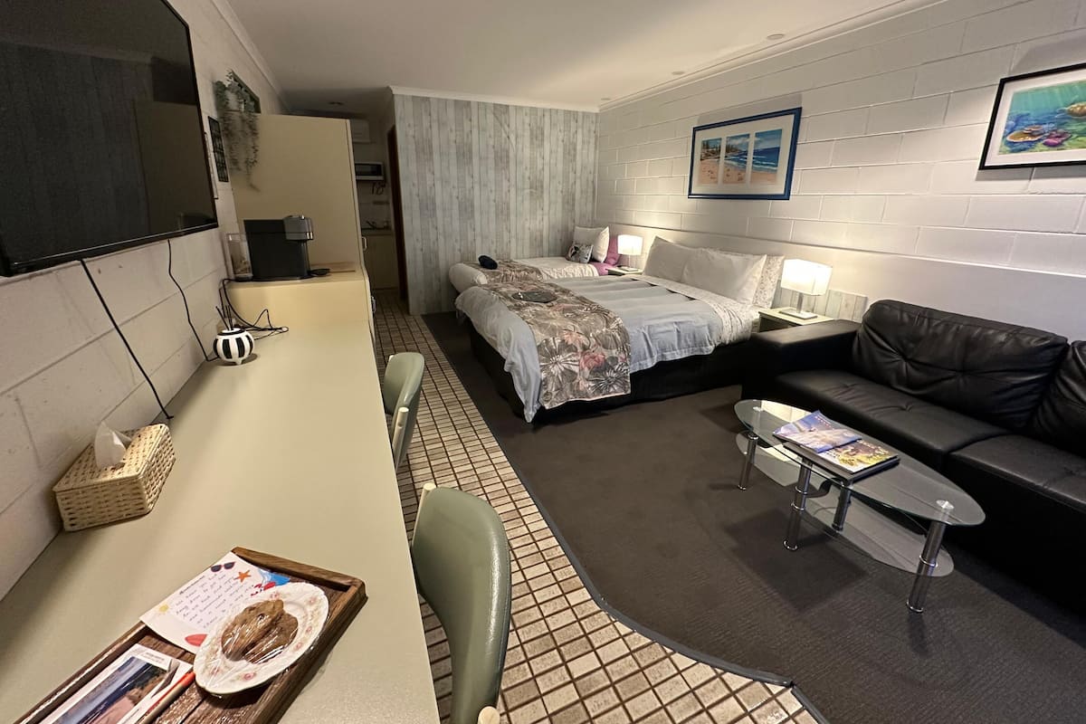 A compact hotel room with a bed, a sofa, a small table, and a TV.