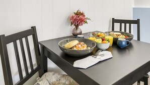 A dining table with a bowl of food, a vase with flowers, and several glasses of juice. - Sandbar Motel (Lakes Entrance)