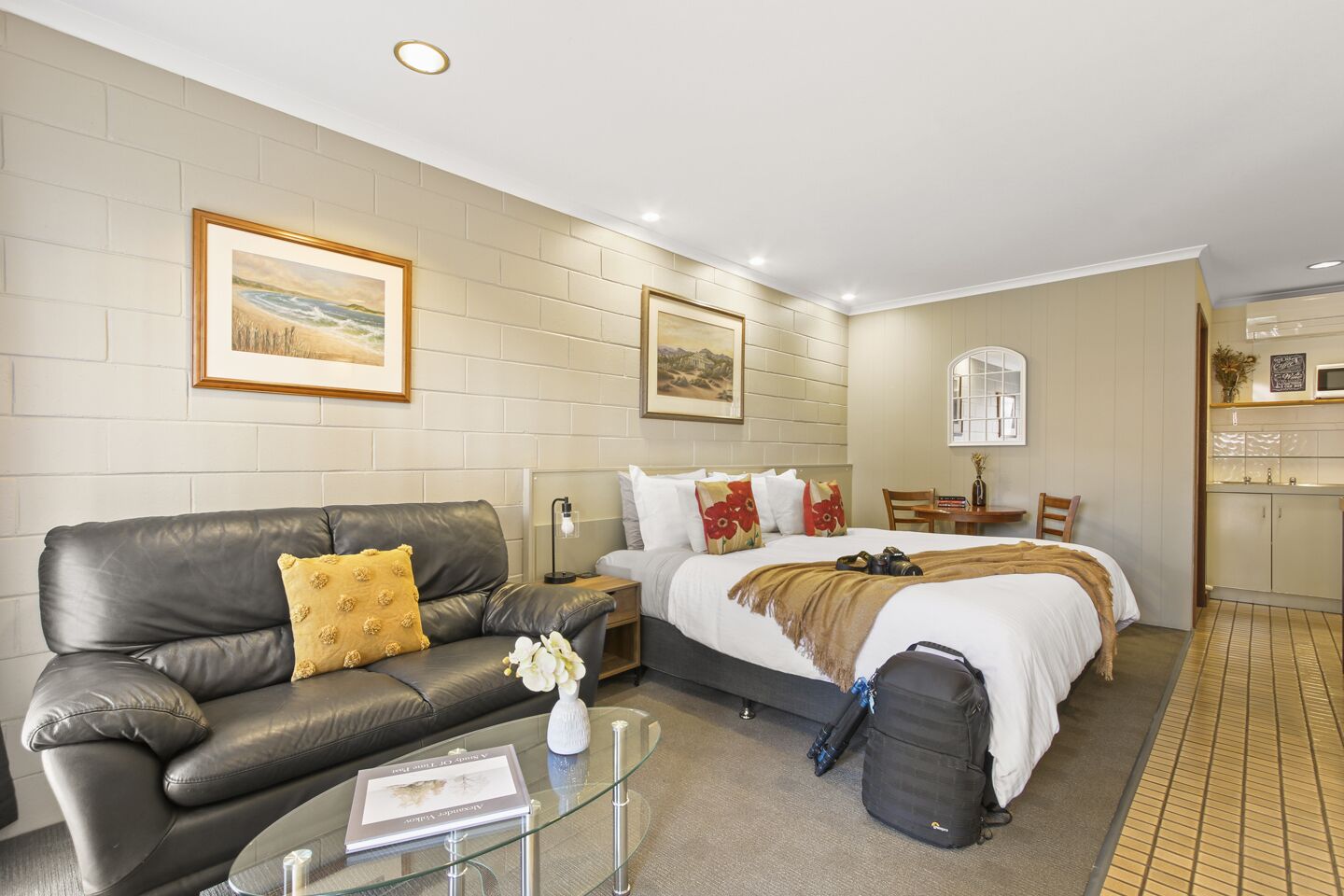 A hotel room with a bed, a leather sofa, a glass coffee table, and a small desk.