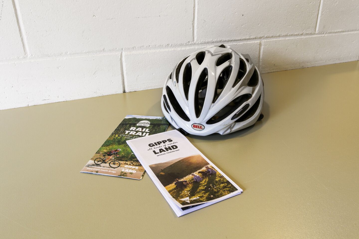 A white bicycle helmet and two travel brochures on a beige surface.