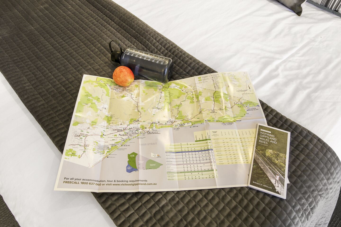 A bed with a map, a water bottle, and a brochure on a quilted bedspread.