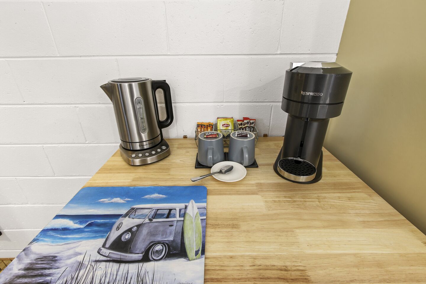 Una encimera de cocina con una cafetera, un hervidor y un soporte para cápsulas de café.