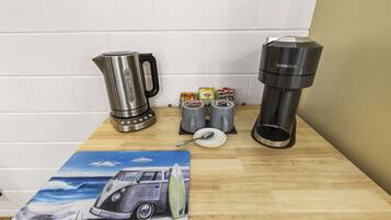 Una encimera de cocina con una cafetera, un hervidor y un soporte para cápsulas de café.