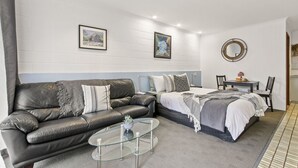 A modern bedroom with a leather sofa, a glass coffee table, a bed with a white headboard, and two framed pictures on the wall. - Sandbar Motel (Lakes Entrance)