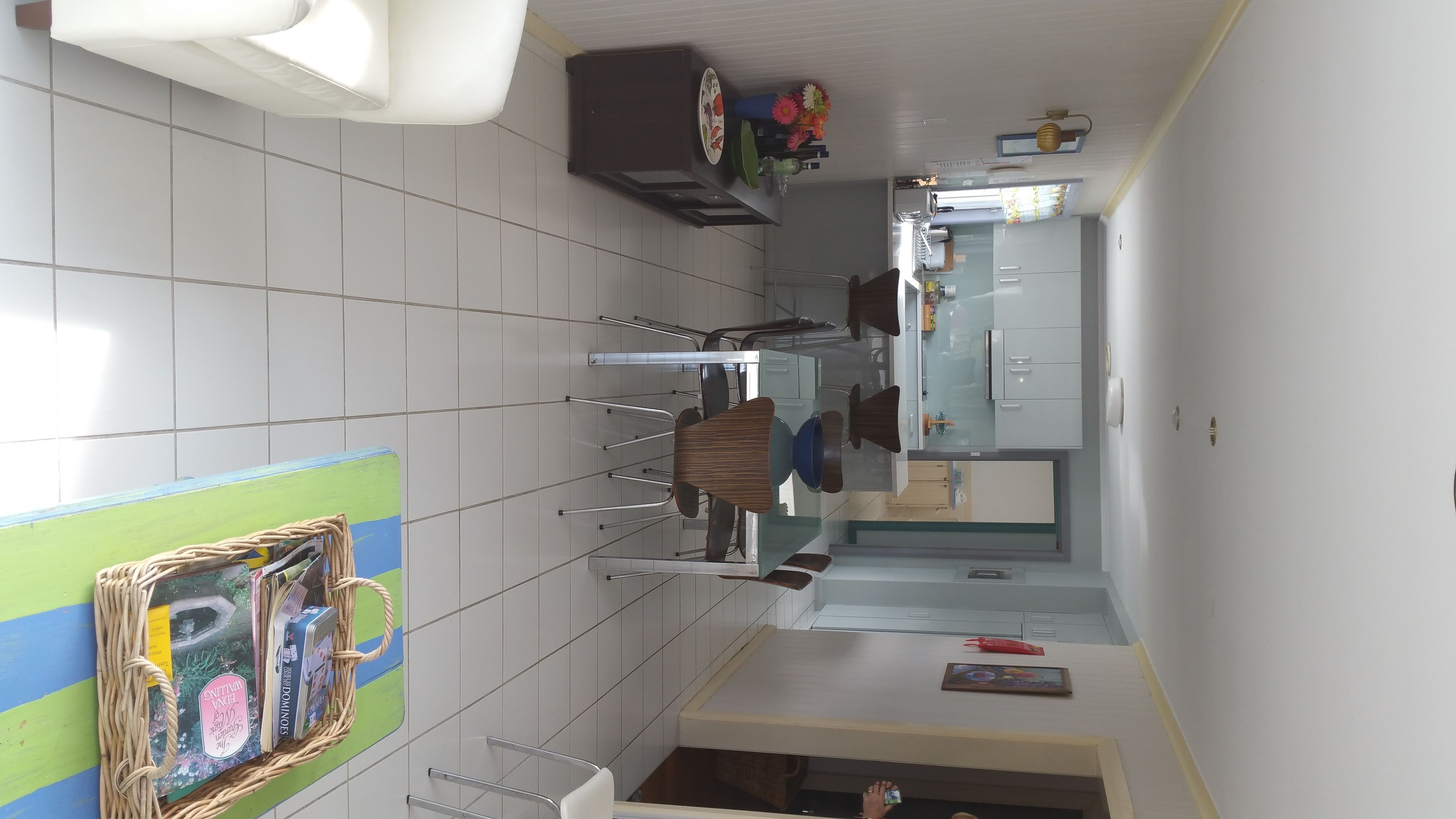 Eine Küche mit weißen Fliesen, einem Esstisch mit Stühlen, einem Kühlschrank und einer kleinen Kochinsel mit Spüle.