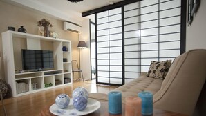 A living room with a sofa, a TV, a bookshelf, and a table with decorative items. - Newtown Mews (Newtown)