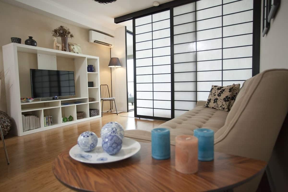 A living room with a sofa, a TV, a bookshelf, and a table with decorative items.
